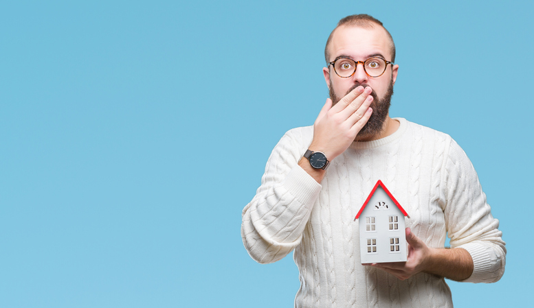 A man covering his mouth while holding a miniature house