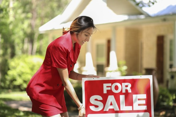 A female real estate agent posting a 'for sale' signage to sell your home fast